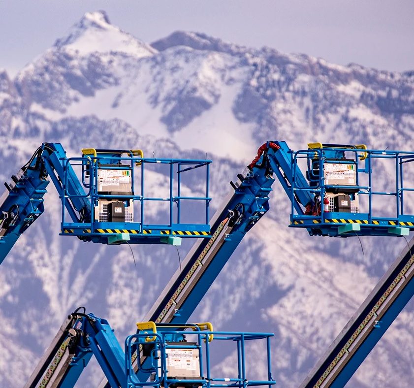 Three blue aerial lifts with a mountain range in the background.